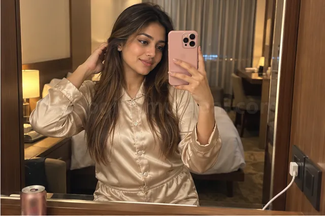 A woman in a champagne satin night set taking a mirror selfie in a hotel room