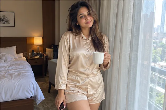 A woman in a satin night set holding a cup of tea by a hotel window in the morning